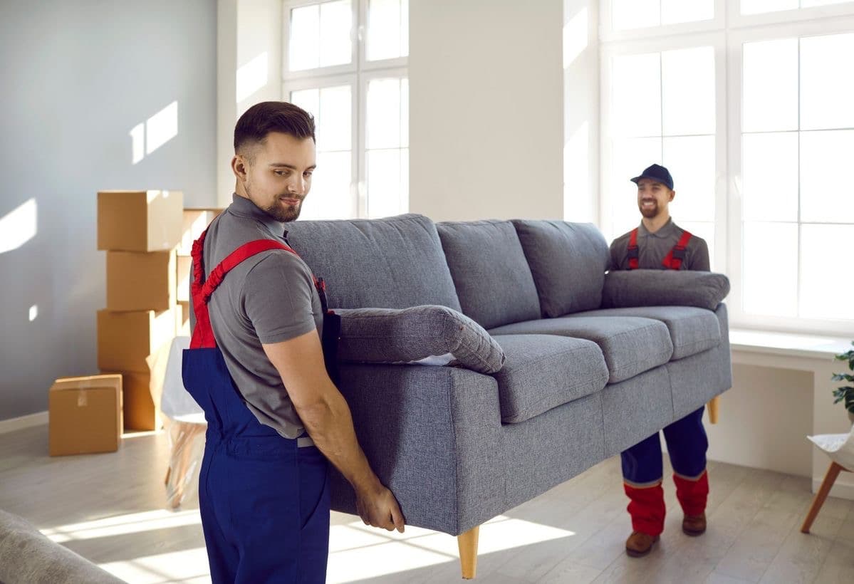 Deux déménageurs portent un canapé dans un appartement lumineux