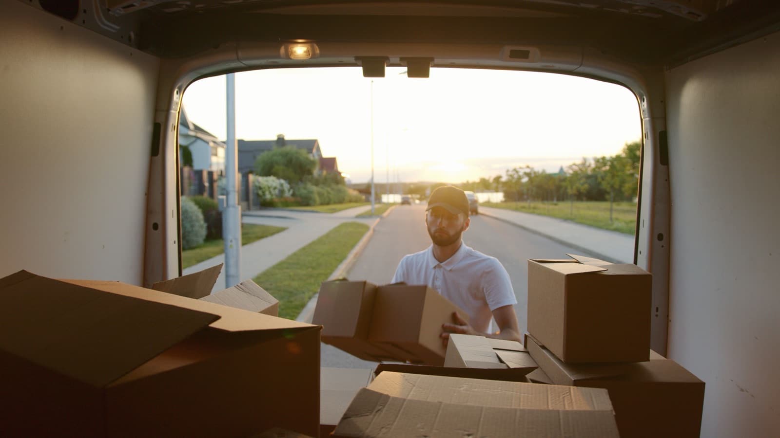 Vue depuis l'intérieur d'une camionnette chargée de cartons, un homme en porte un de plus à l'arrière