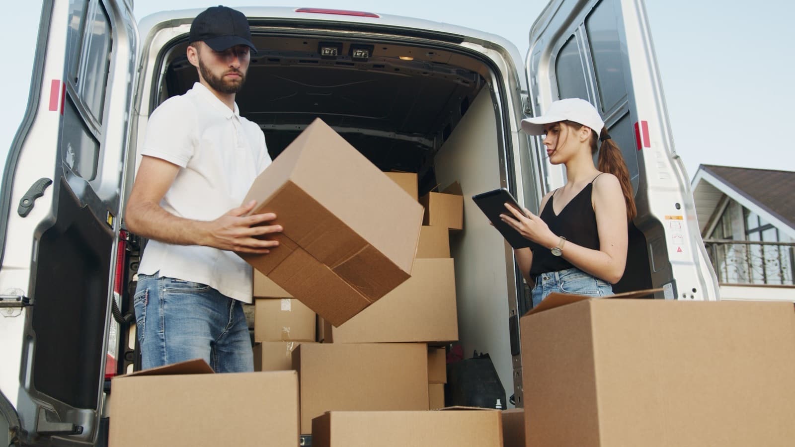 Deux personnes déchargent des cartons à l'arrière d'une camionnette de déménagement aux portes ouvertes