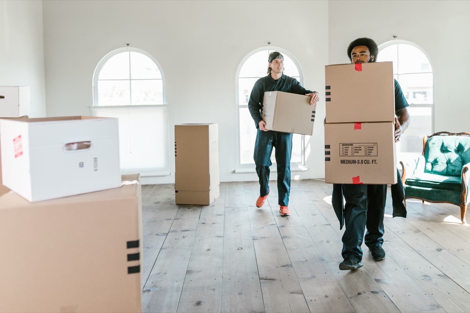 Deux déménageurs portant des cartons dans un appartement vide aux grandes fenêtres cintrées
