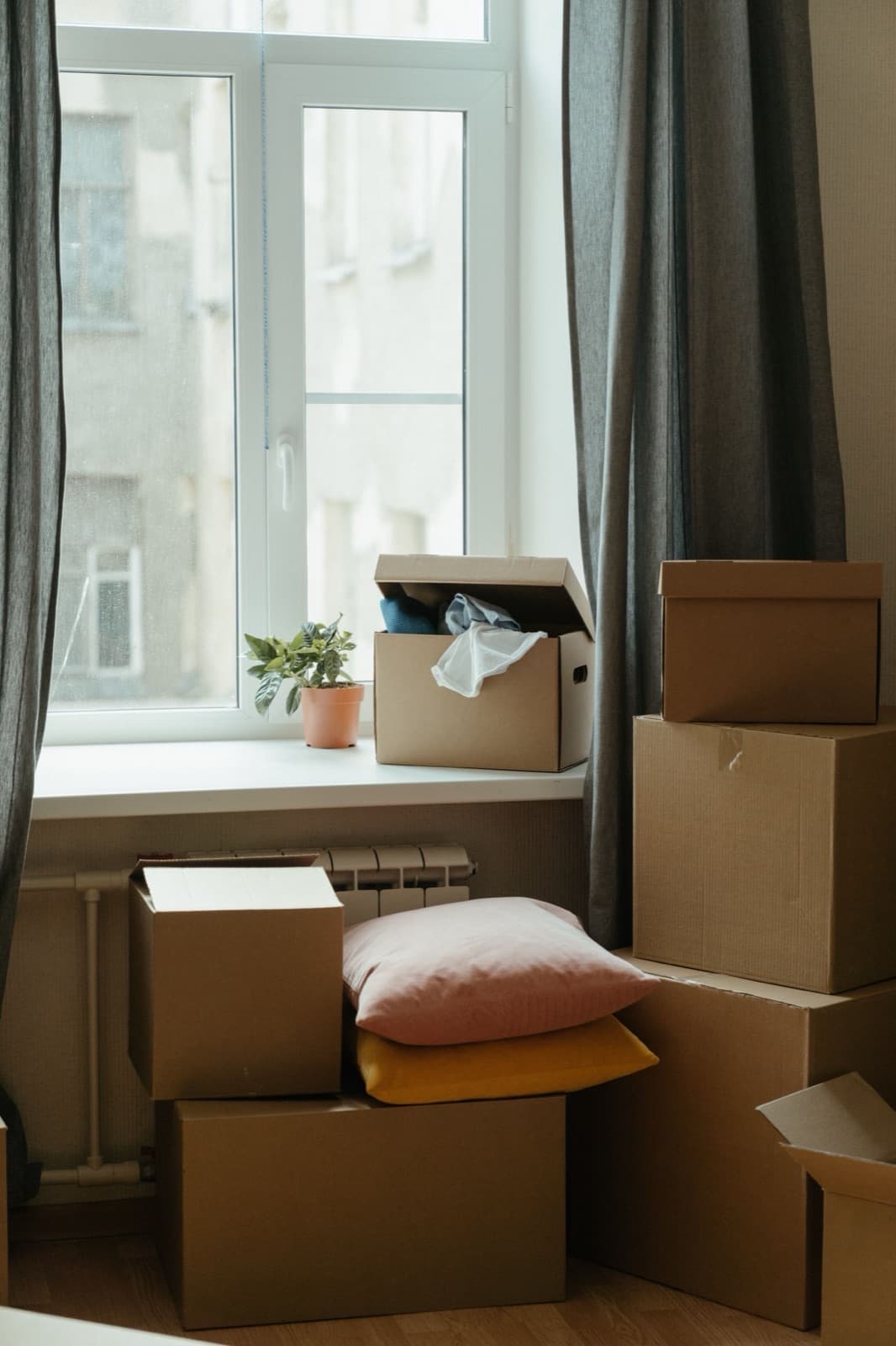 Pile de cartons de déménagement fermés et de coussins, prêts à partir près d'une fenêtre