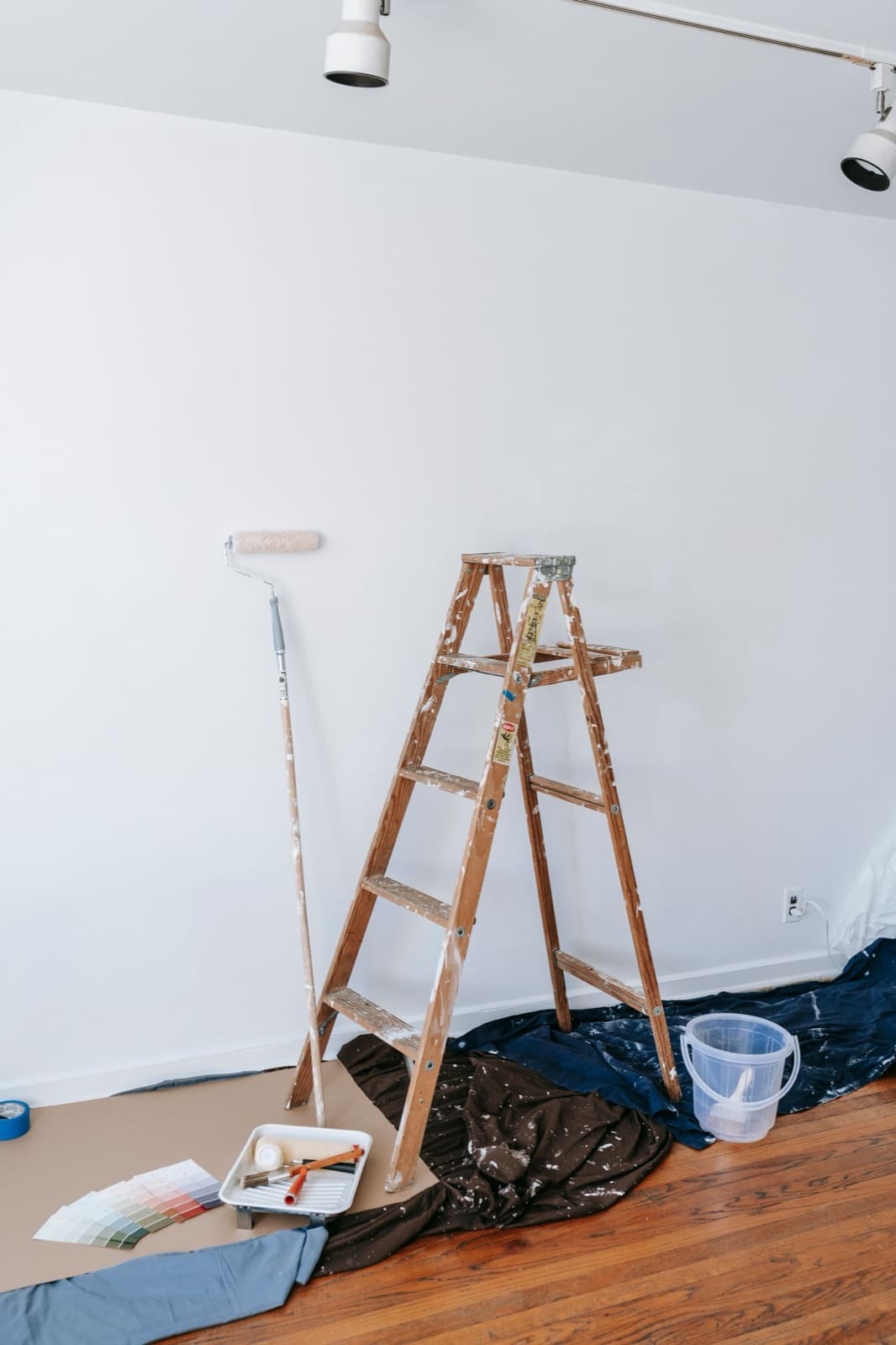 Échelle, bâches et pots de peinture installés dans une pièce vidée avant les travaux