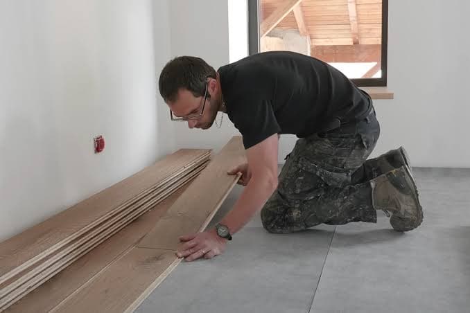 Poseur à genoux qui assemble des lames de parquet le long d'un mur